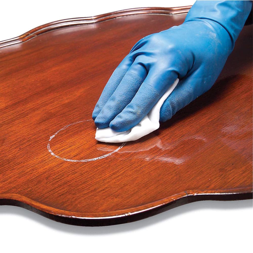 A gloved hand cleaning a coffee table. 
