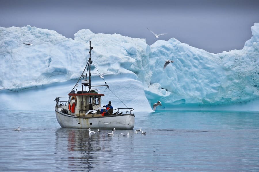 Fishermen are photographed navigating around blue icebergs.