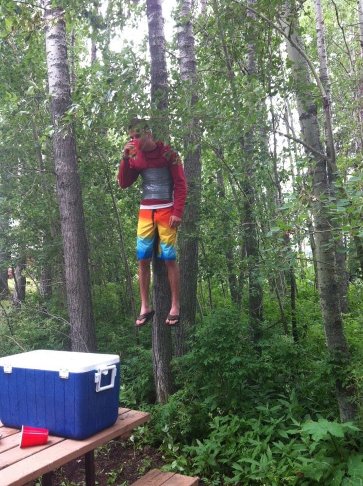 teenager hanging on a tree by duct tape around his stomach, drinking from a cup