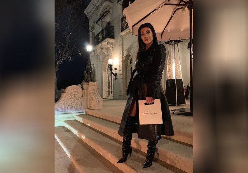 Kourtney Kardashian dressed in all black holding a Victoria Beckham bag. 