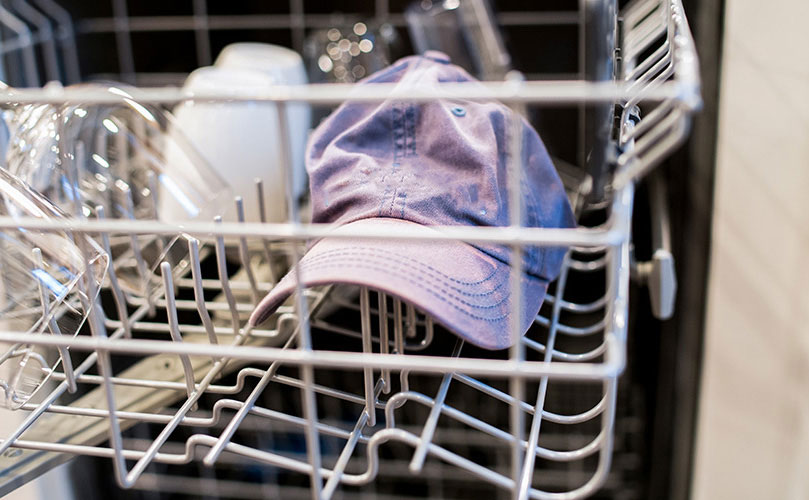 A baseball cap surrounded by glasses in the dishwasher 