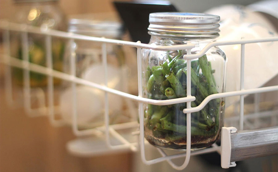 String beans and spices inside of a mason jar sitting on a dishwasher rack 