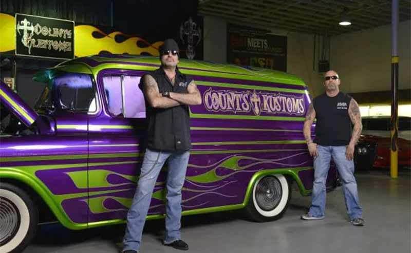 Danny and Kevin standing in front of a car that is purple with green flames and says Counts Kustoms on it 