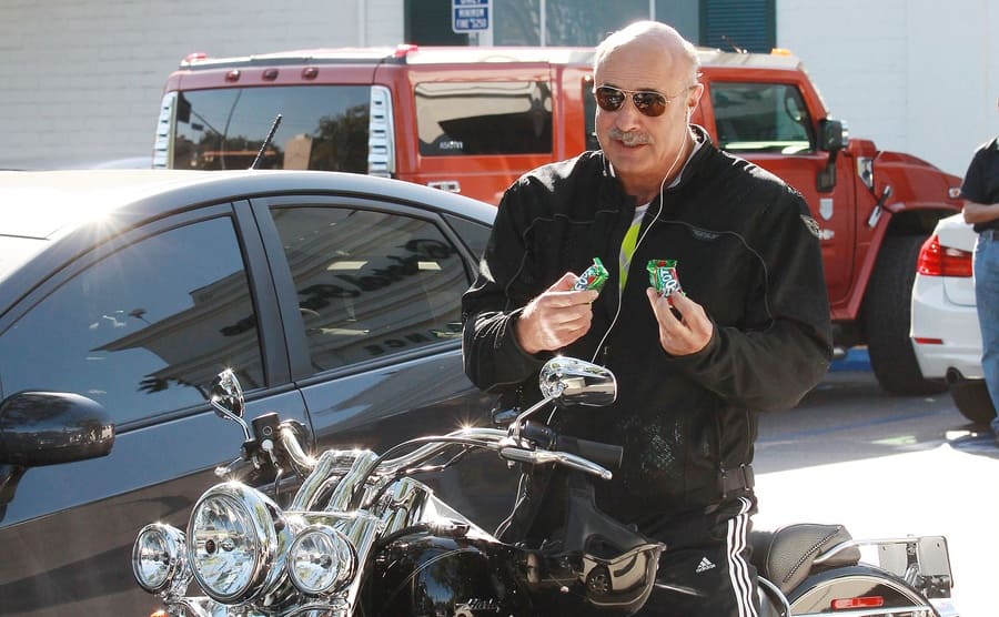 Dr. Phil sitting on a motorcycle holding fruit by the foots 