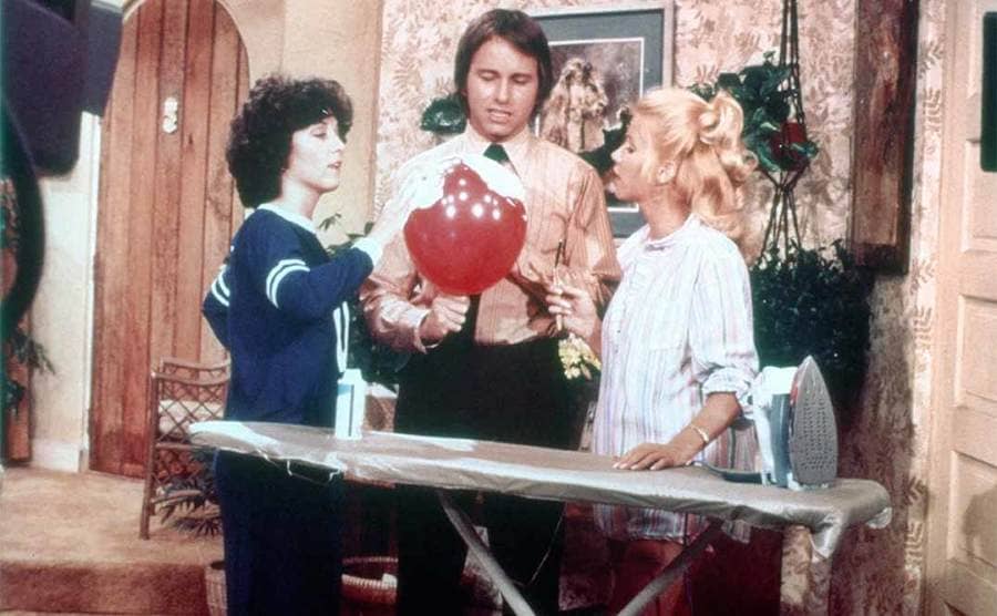 Joyce DeWitt, John Ritter, and Suzanne Somers putting shaving cream on a blown-up balloon in an episode of Three’s Company 