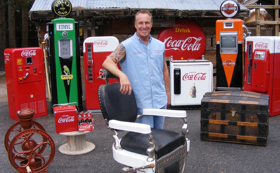 Rick standing in front of an old barbers chair with old gas pumps and coca-cola machines behind him 