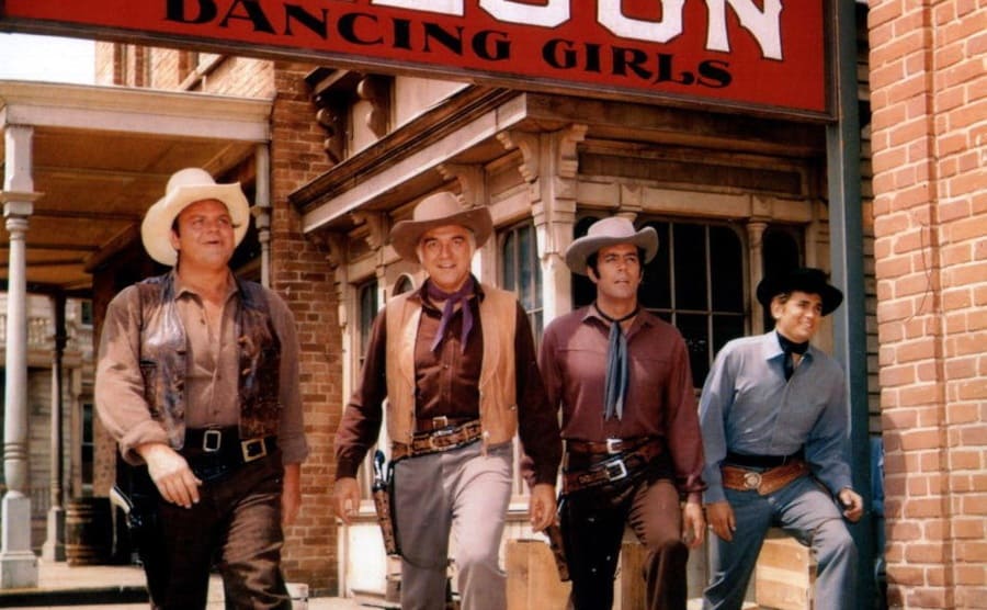 Dan Blocker, Pernell Roberts, Michael Landon, and Lorne Greene posing together in front of a sign that says ‘Saloon dancing girls’