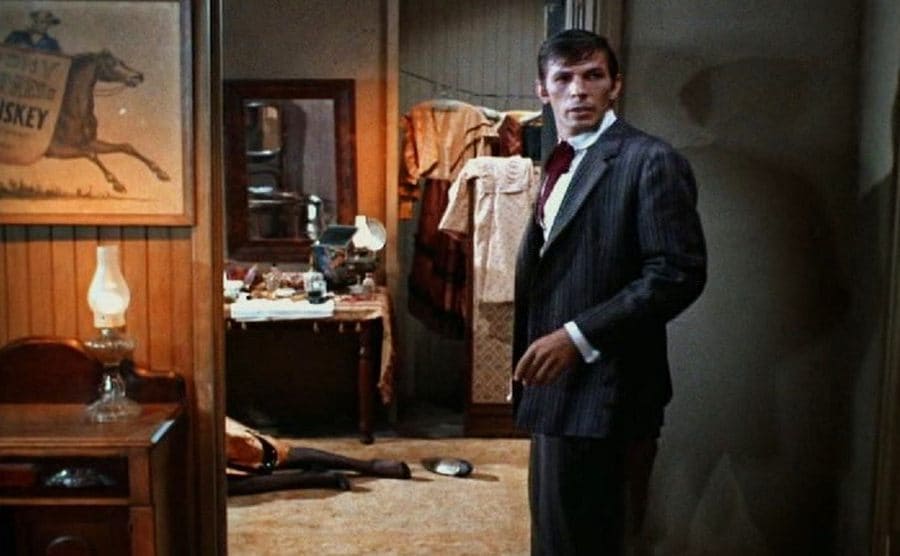 Leonard Nimoy standing in a doorway with a woman’s legs sprawled out on the floor 