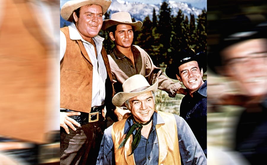 Dan Blocker, Michael Landon, Lorne Greene, and Pernell Roberts posing together with trees and mountains behind them 