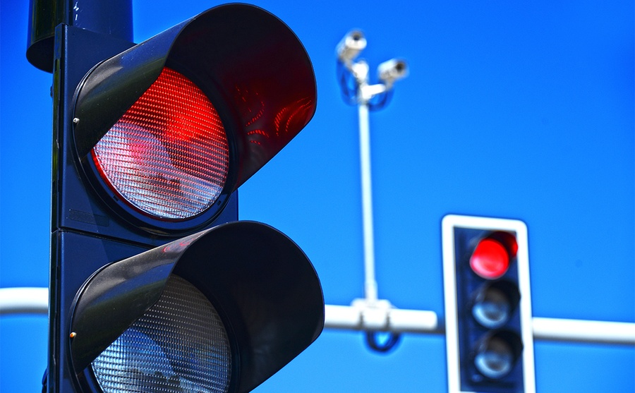 A red light shining on traffic lights in front of a blue sky 