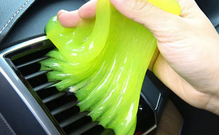 A person using yellow slime to remove dust from an air conditioning vent in a car 