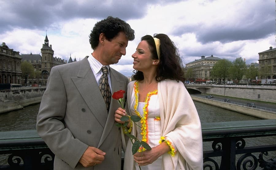 Charles Shaughnessy and Fran Drescher holding a rose on a bridge in the show The Nanny 