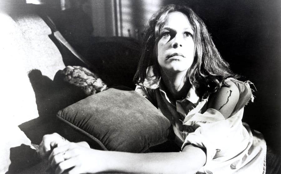 Jamie Lee Curtis kneeling next to a couch in the film Halloween 