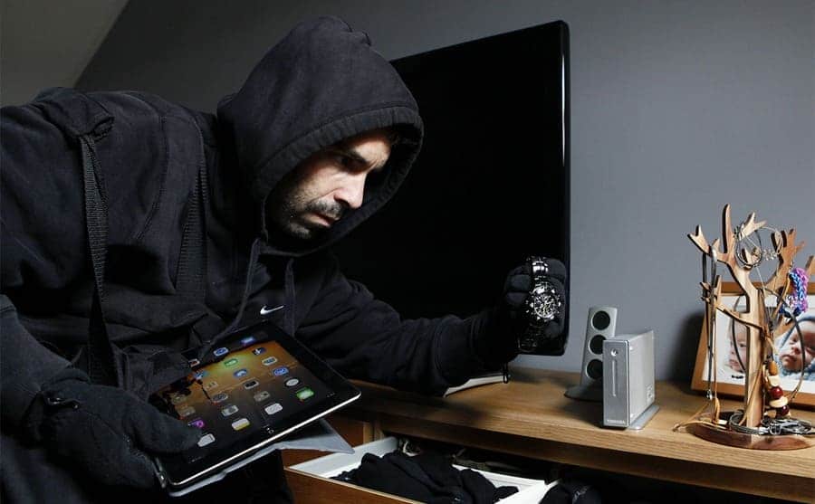 A burglar picking up an iPad and watch from a home desk 