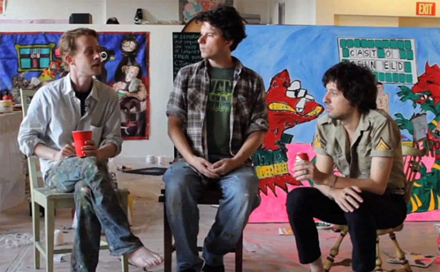 Macaulay Culkin, Adam Green y Toby sentados con obras de arte a su alrededor