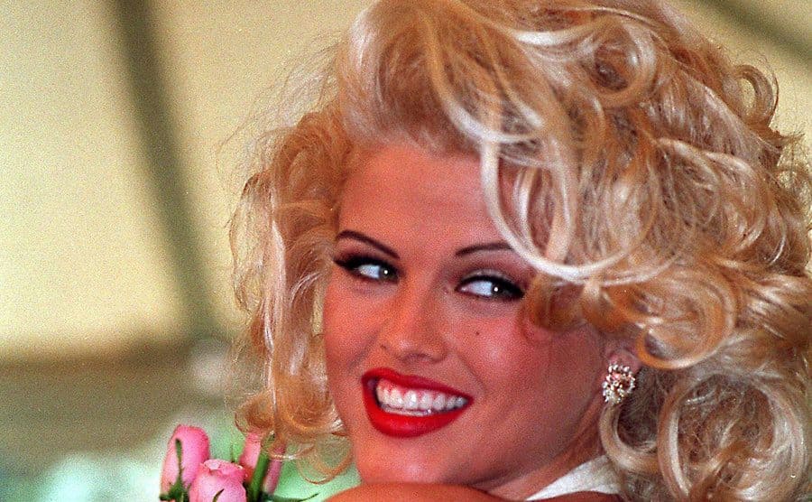 Anna Nicole Smith posing with pink roses looking back over her shoulder 