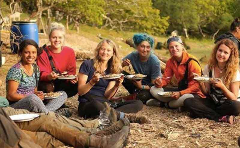 Contestants sitting around the dirty ground eating dinner 
