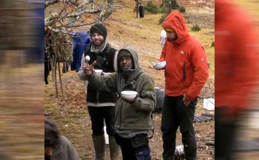 Three contestants hanging around in warm gear holding bowls and spoons 