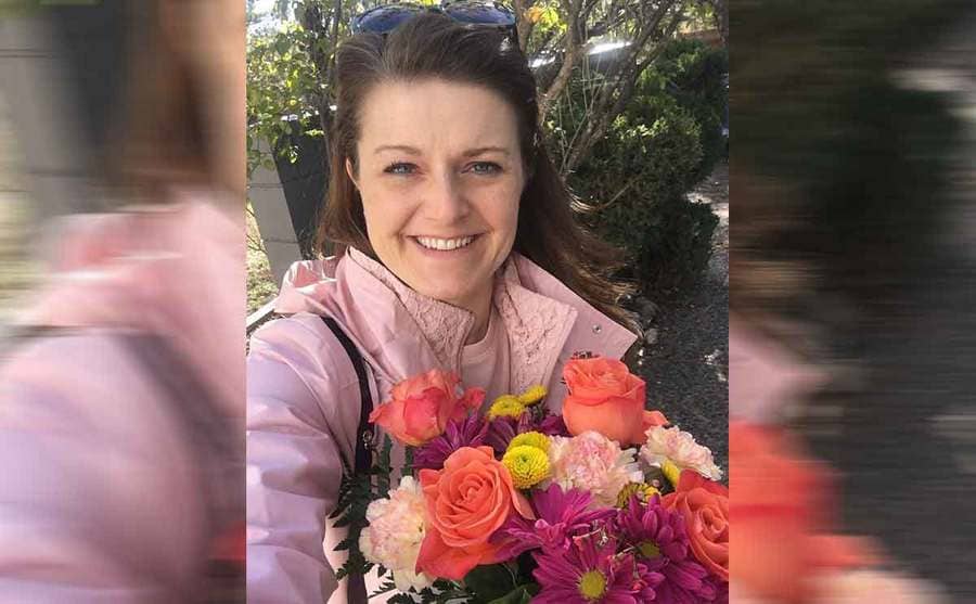 Robyn Brown holding a bouquet of flowers for a selfie outdoors 