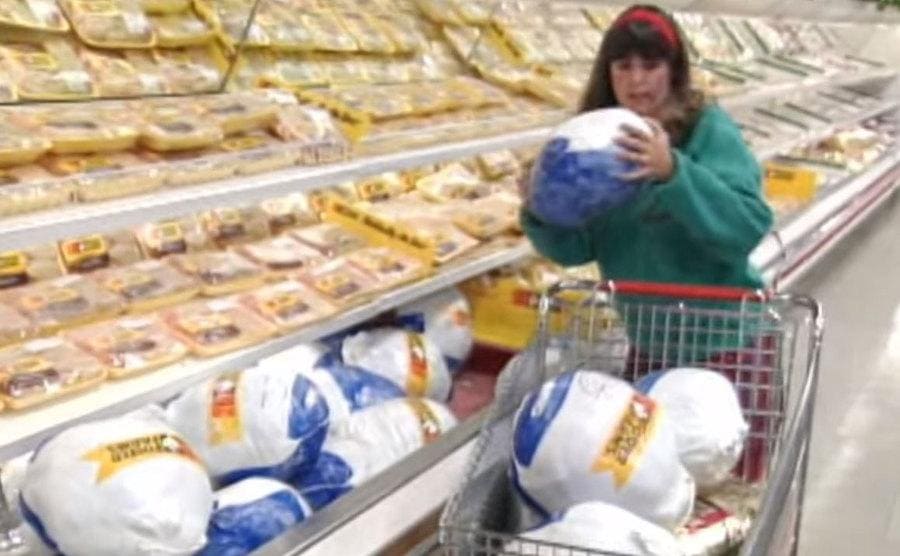 A woman competing on the show grabbing and tossing a full turkey into her cart.