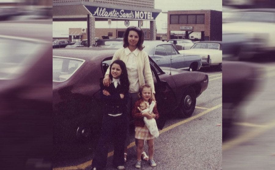 Julia Louis-Dreyfus with her mother and sister standing in front of an old car in the parking lot of the Atlantic Sands Motel circa 1970 