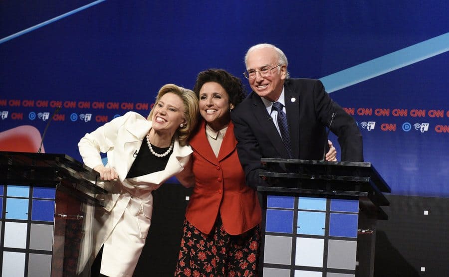 Kate McKinnon, Julia Louis-Dreyfus, and Larry David posing behind podiums in a scene from a recent political Saturday Night Live sketch 