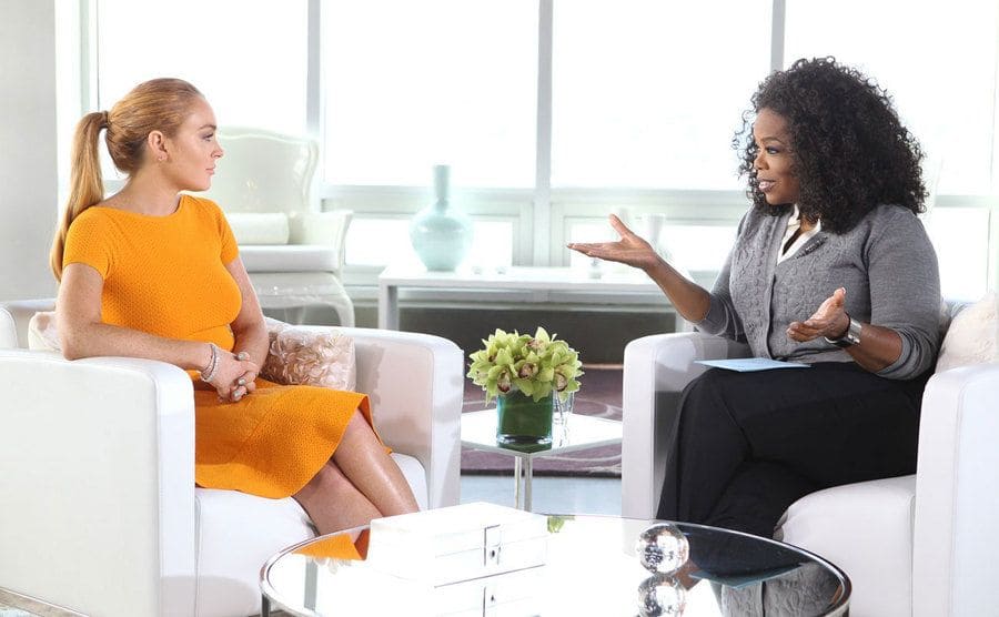 Lindsay Lohan being interviewed by Oprah in a talk show setting with all-white furniture 