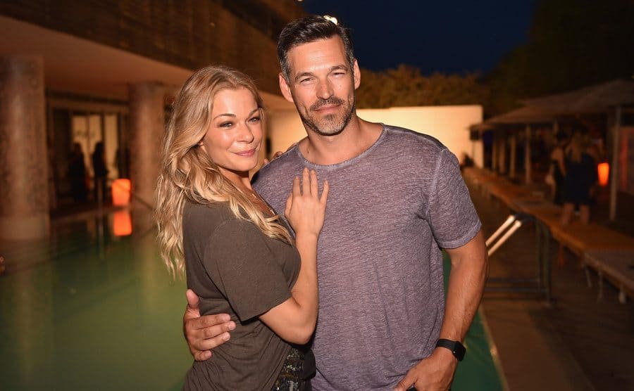 LeAnn Rimes and Eddie Cibrian posing in a backyard event next to a pool 