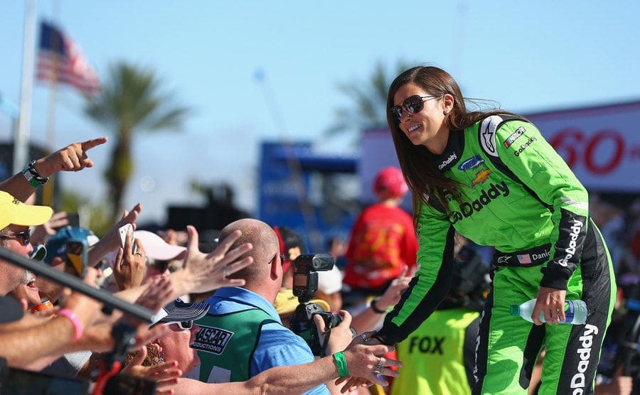 Danica Patrick high-fiving fans while wearing her racing suit 