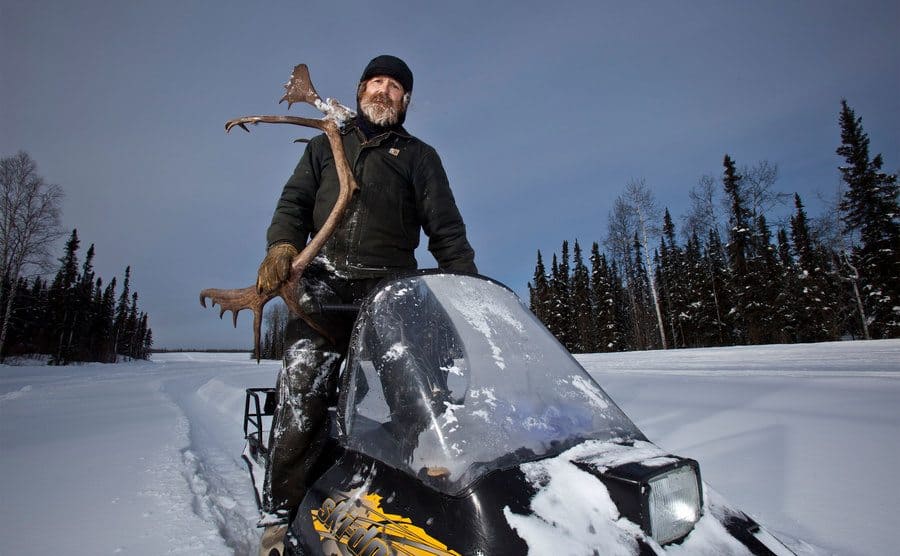 Marty riding his snowmobile while carrying moose antlers.