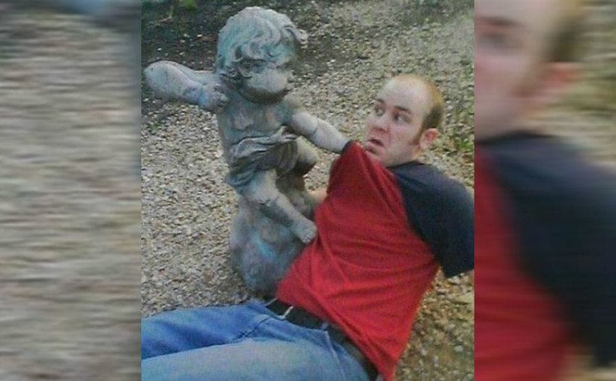 Graciosa imagen de chico posando junto a una estatua en forma de angelito enojado