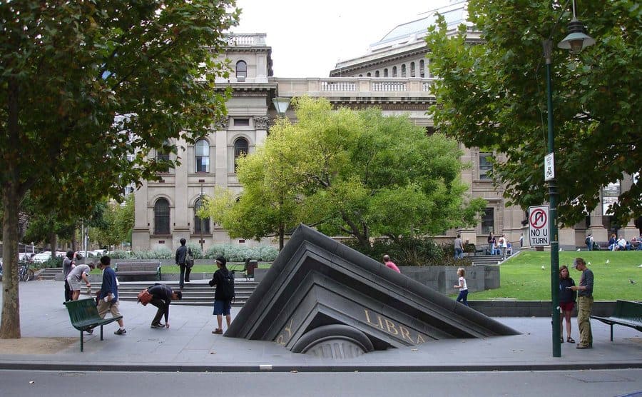 Escultura de edificio que se hunde fuera de la Biblioteca Estatal (Melbourne, Australia)