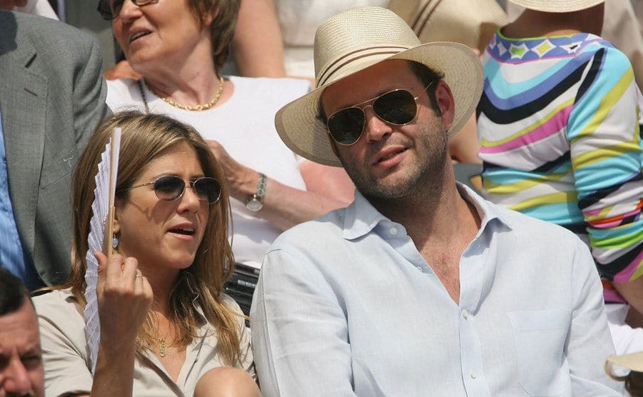 Jennifer Aniston fanning herself while sitting with Vince Vaughn at a sporting event 