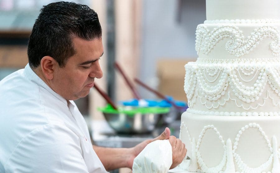 Buddy piping delicate designs into a white four-tiered wedding cake 