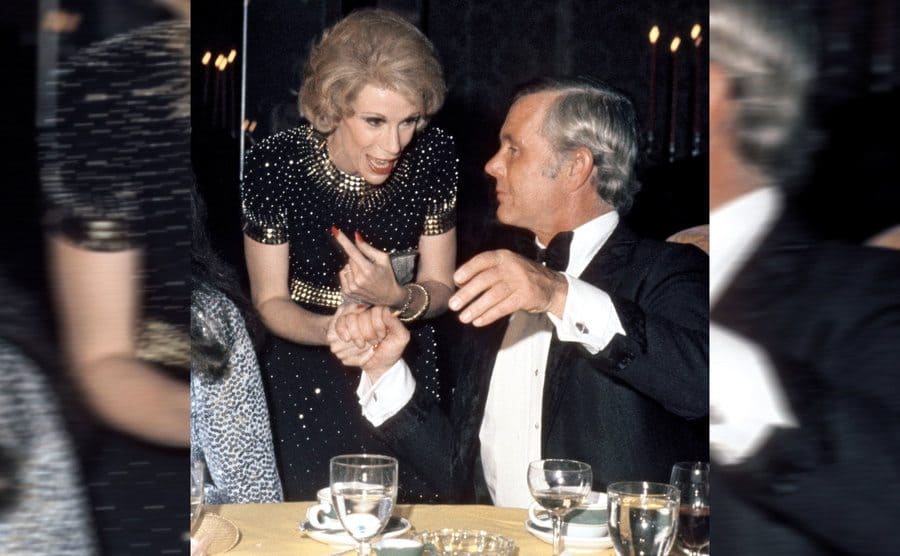 Joan Rivers and Johnny Carson having a conversation over the dinner table at an event 