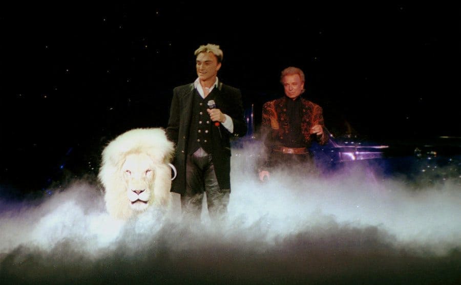 Siegfried and Roy performing onstage with a lion. 