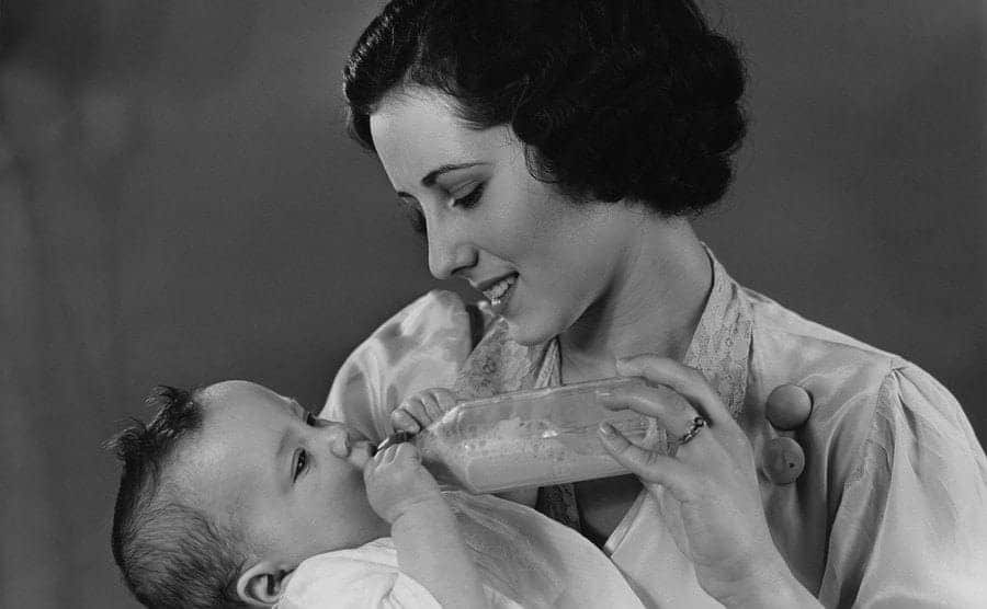 A mother is feeding a milk bottle to a sleepy baby 