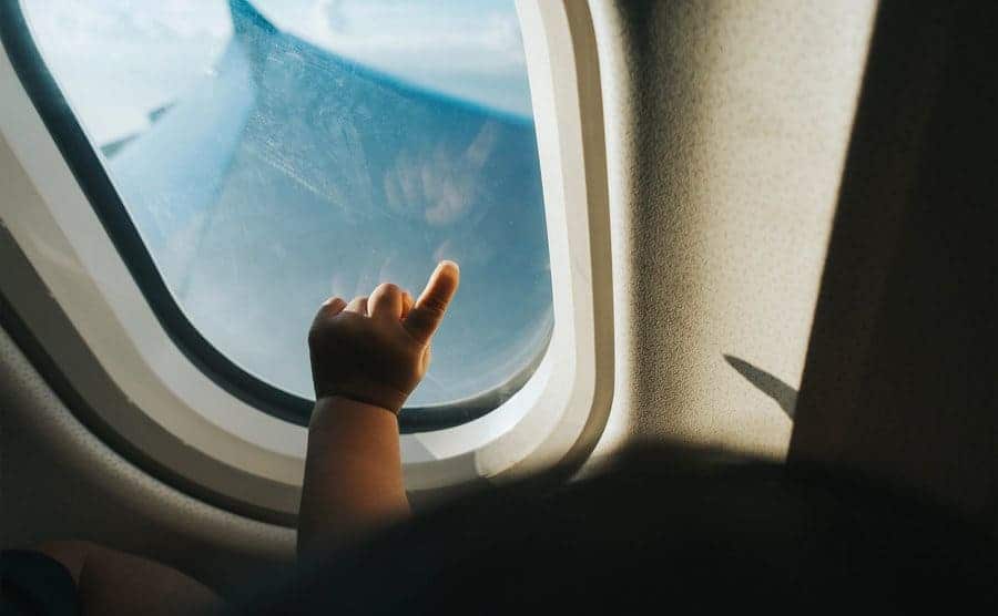 Cropped hand of a toddler pointing at the airplane window against the blue sky while traveling.