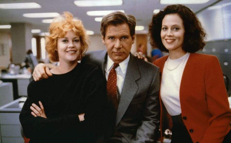 Melanie Griffith, Harrison Ford, and Sigourney Weaver posing in an office setting on the set of Working Girl 