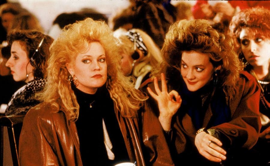 Melanie Griffith and Joan Cusack sitting in a crowded waiting room 