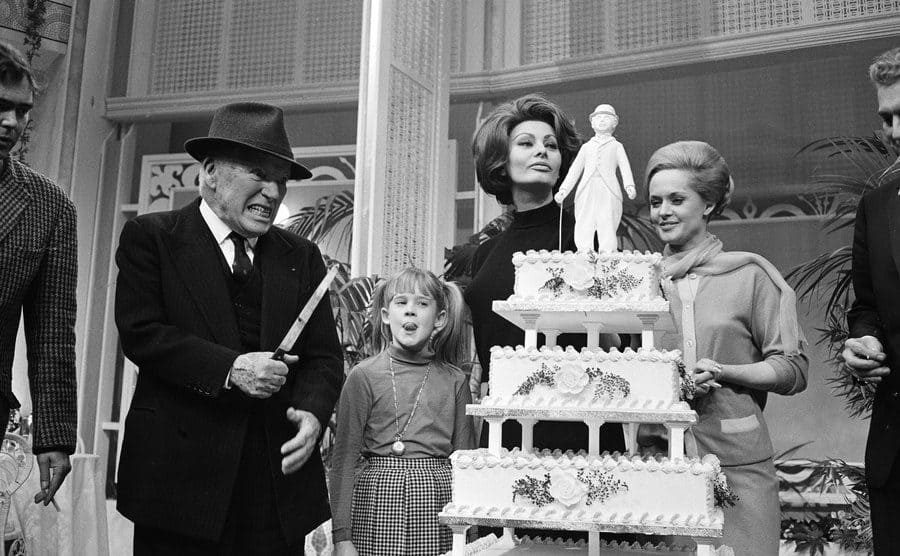 Charlie Chaplin, Melanie Griffith, Sophia Loren, and Tippi Hedren standing around a tall cake celebrating Chaplin’s birthday 