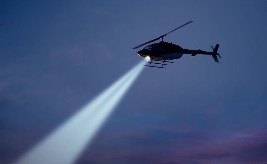 Police helicopter shining a light beam in the dark sky.