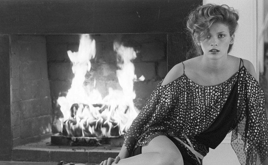 Gia Carangi as she sits in front of a lit fireplace.