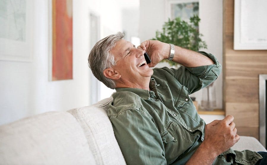 A man talking and laughing on a cellphone at home.