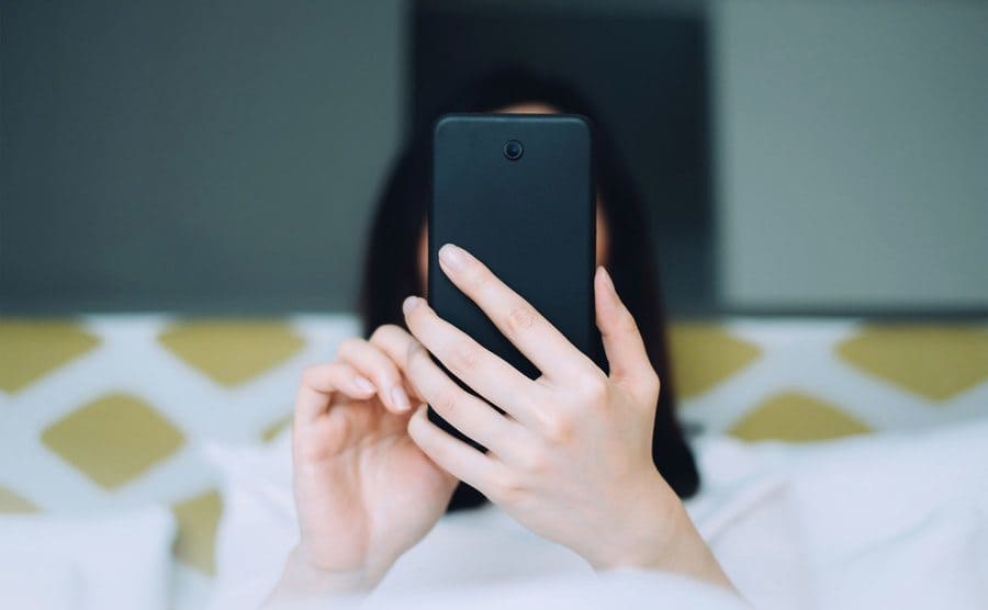 A portrait of a woman using her mobile phone while lying on the bed.