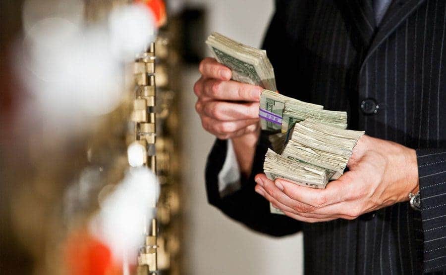 A man is holding a big stack of US dollar bills as he stands by safety deposit boxes.