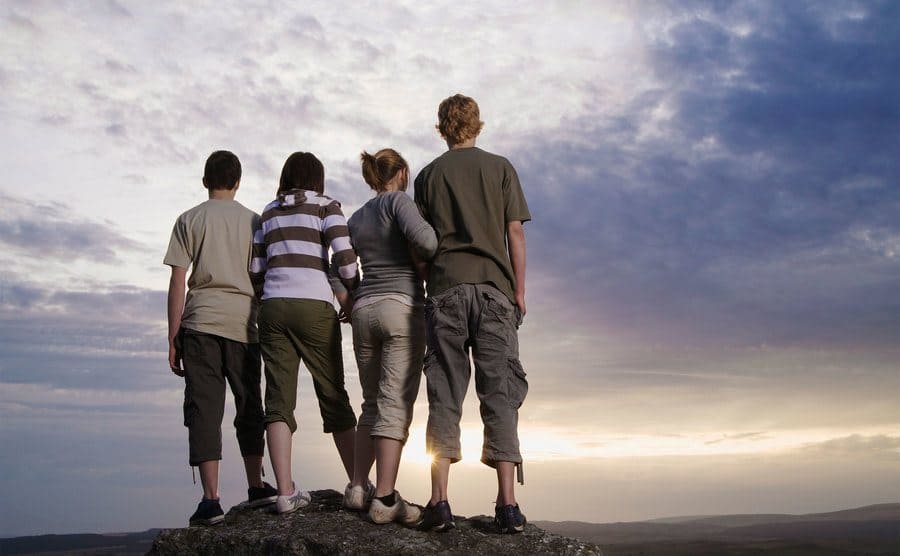 Four Teenagers are standing on a mountain top with their backs to the camera. 