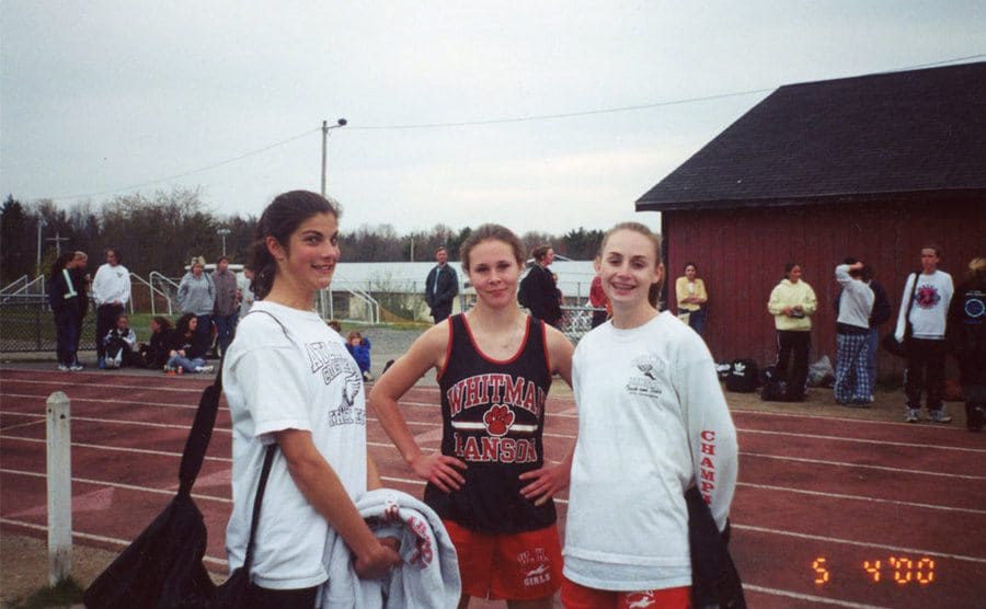Maura is standing beside two friends on the track field.