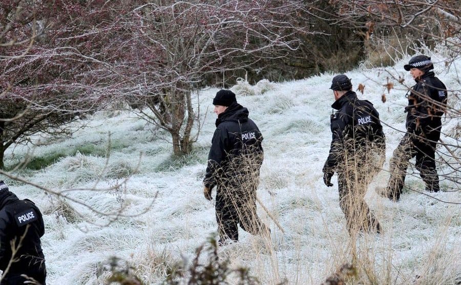 Police officers searching the snowy woods. 