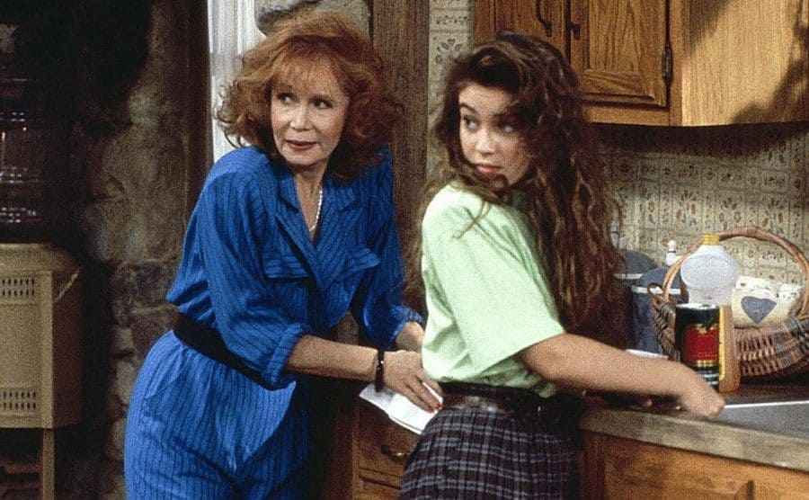 Alyssa Milano and Katherine Helmond, as Sam and Mona, are looking over their shoulders while standing in the kitchen. 